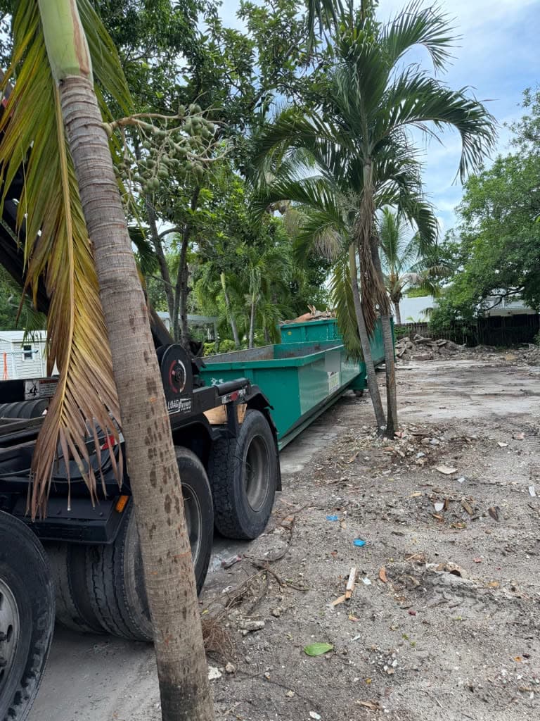 Roll-off truck and dumpster at a cleared residential lot with palm trees