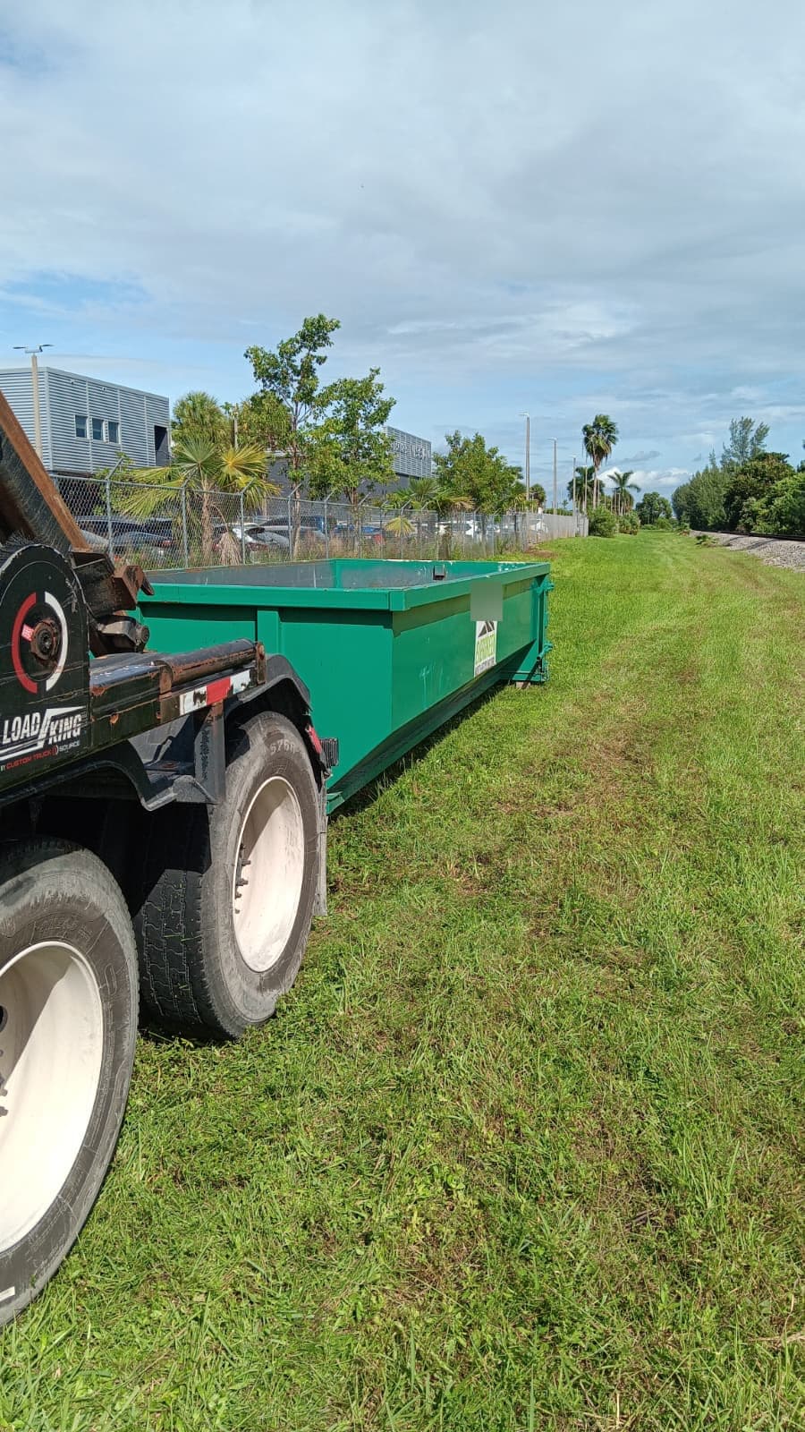 Roll-off truck delivering a green dumpster onto a grass lot